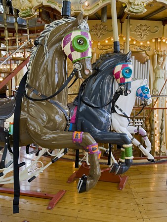 Dva malovaní dřevění koně na kolotoči, umístění vedle sebe, s ozdobnými detaily a barevnými postroji