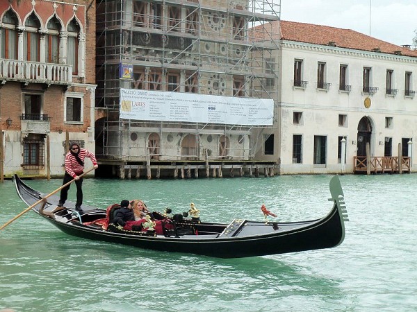 Gondoliér veze turisty po kanálu mezi historickými budovami v Benátkách