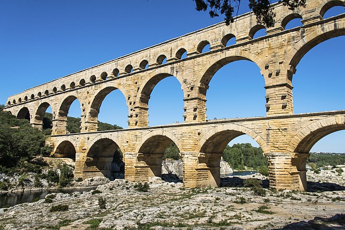 Kamenný akvadukt s několika řadami oblouků nad skalnatou krajinou