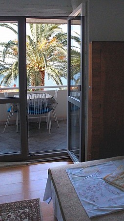 Pokoj s postelí a dveřmi na balkon, kde stojí stůl se židlemi