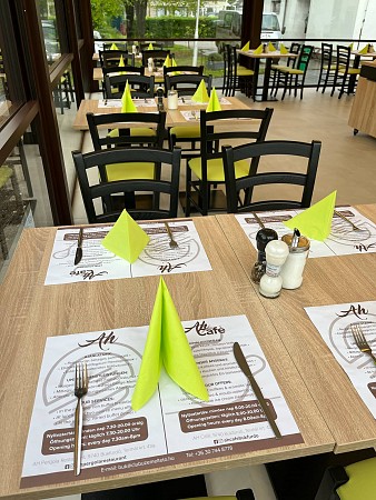 Stoly v restauraci jsou prostřené se zelenými ubrousky, jídelními sety a příbory