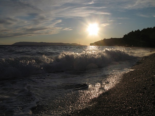 Mořské vlny narážející na oblázkovou pláž v Tučepi při západu slunce