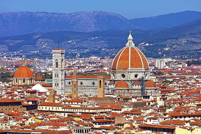 Historické město s červenými střechami, mezi nimiž vystupuje katedrála s velkou cihlovou kopulí a vysokou zvonicí
